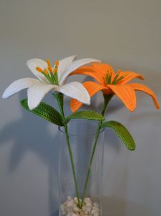 three white and orange flowers in a glass vase filled with rocks, water and pebbles