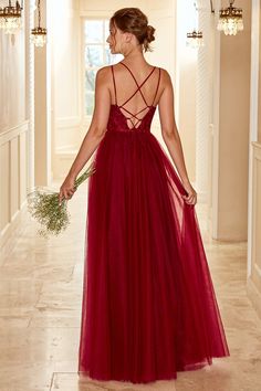 a woman in a long red dress is walking down the hall holding a flower bouquet