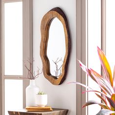 a wooden mirror hanging on the wall next to a table with a vase and potted plant