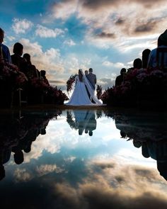 a bride and groom are standing in front of the water at their wedding ceremony with clouds reflecting on the ground