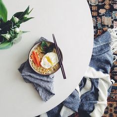 a bowl of food on a table with chopsticks and a potted plant