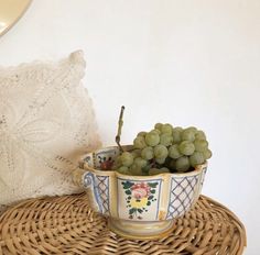 a bowl filled with grapes sitting on top of a wicker table next to a pillow