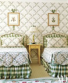 two beds in a room with green and white bedding on the covers, one has a lamp next to it