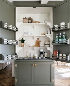 a kitchen with gray cabinets and shelves filled with dishes on top of wooden flooring