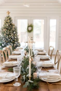 a dining room table set for christmas dinner with candles and greenery on the table