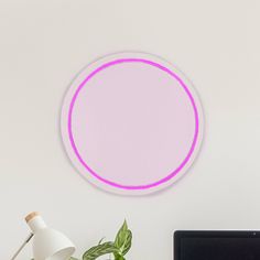 a laptop computer sitting on top of a desk next to a pink circle wall light