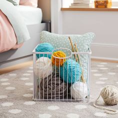 a basket filled with balls of yarn next to a bed