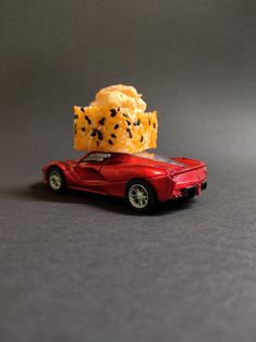 a toy car with some food on top of it's roof, sitting in front of a gray background