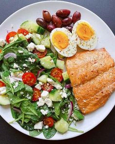 a white plate topped with salad and an egg on top of it next to a croissant