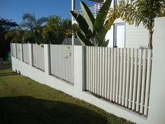 a white picket fence in front of a house with trees and bushes on the side