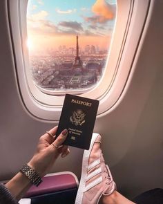 a person holding a passport in front of an airplane window with the eiffel tower in the background