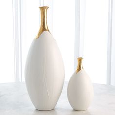 two white and gold vases sitting on top of a marble table next to each other