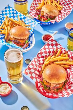 three plates with sandwiches and french fries on them next to two glasses of beer, ketchup and mustard