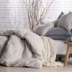 an unmade bed with pillows and blankets on it in front of a brick wall