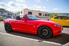 a red sports car parked in a parking lot next to another yellow car and trailer