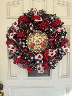 a red and black wreath with ladybugs on the front door, welcome home