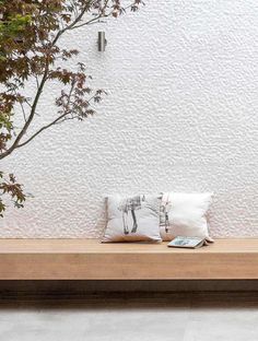 a wooden bench sitting next to a tree on top of a cement floor under a white wall