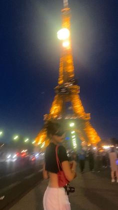 a woman standing in front of the eiffel tower at night with her cell phone