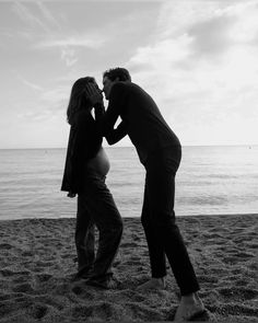 a man and woman kissing on the beach by the water's edge in black and white