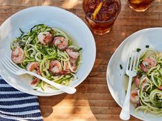 two white bowls filled with pasta and shrimp on top of a wooden table next to drinks