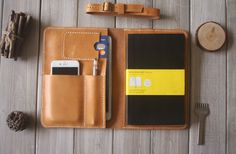 a leather wallet with a notepad, pen and pencil on it next to other items