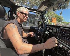 a man driving a truck with tattoos on his arm and shoulder, in the drivers seat