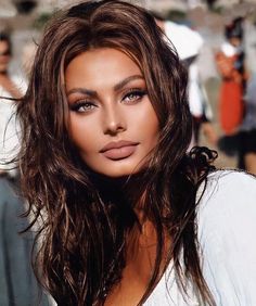 a woman with long brown hair and blue eyes posing for a photo in front of a crowd