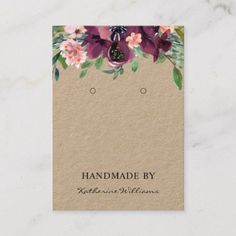 a business card with purple flowers and greenery on the bottom, in front of a white marble background