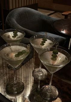 three martini glasses with olives in them sitting on a table