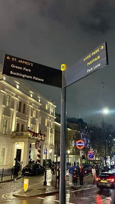 a street sign on the side of a city street at night with people walking by