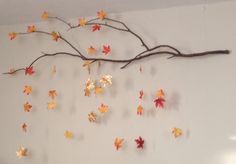 a branch with autumn leaves hanging from it's side in front of a white wall