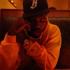 a man sitting at a table talking on a cell phone while wearing a baseball cap