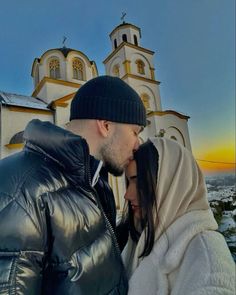 a man and woman standing next to each other in front of a church at sunset