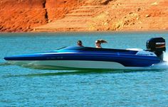 a blue and white speed boat with two people in it on the water near some cliffs