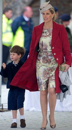 a woman in a red coat and hat walking next to a small boy