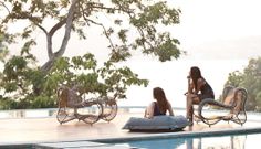 two women sitting on the edge of a swimming pool with chaise lounges in front of them