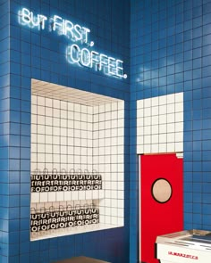 a blue and white tiled wall with a red door in front of it that says but first, coffee