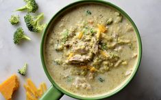 broccoli and cheese soup in a green bowl on a white surface with crackers