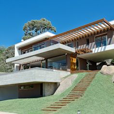 a modern house with stairs leading up to the upper floor and second story, on top of a grassy hill