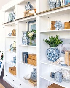 a white bookcase with blue and white vases on it's shelves in a living room