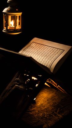 an open book sitting on top of a table next to a lantern