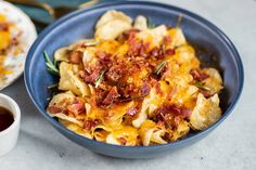 a blue bowl filled with pasta covered in cheese and bacon