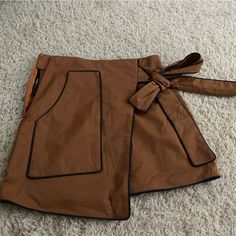 Super Cute Asymmetrical Decorative Side Tie Skirt. Never Worn. Caramel Brown With A Navy/Black Trim With Zipper On The Side Chic Brown Skort For Workwear, Brown Lined Mini Skort, Brown Asymmetrical Skirt For Fall, Chic Brown Skirt With Pockets, High Waist Brown Skirt For Night Out, Brown Mini Skort With Pockets, High Waist Brown Skort With Pockets, Trendy Brown Mini Skirt For Work, Brown Mini Skirt With Pockets