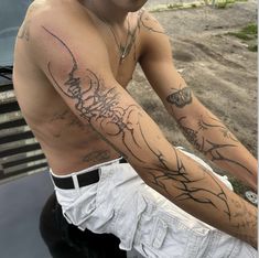 a man with tattoos on his arm sitting on the hood of a car looking off into the distance