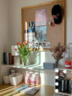 a desk with some flowers and pictures on the wall next to it in front of a mirror