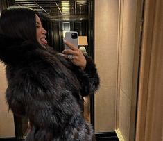 a woman taking a selfie in front of a mirror wearing a fur coat and holding a cell phone