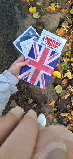 someone is holding up a book with the british flag on it, in front of some leaves