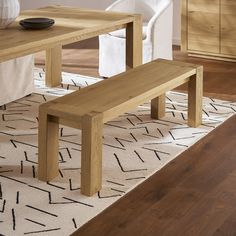 a wooden bench sitting on top of a rug next to a white chair and table