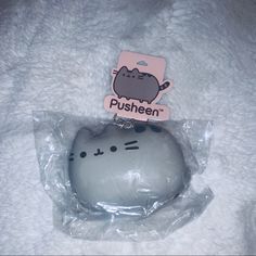 a pusheen cat in a plastic bag on a white blanket with a pink tag