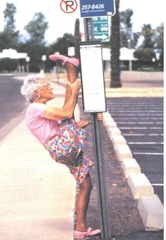 an older woman leaning up against a pole on the side of a road with her feet in the air